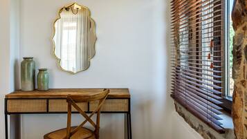 A room with a wooden desk, a chair, a mirror, and a window with wooden blinds.