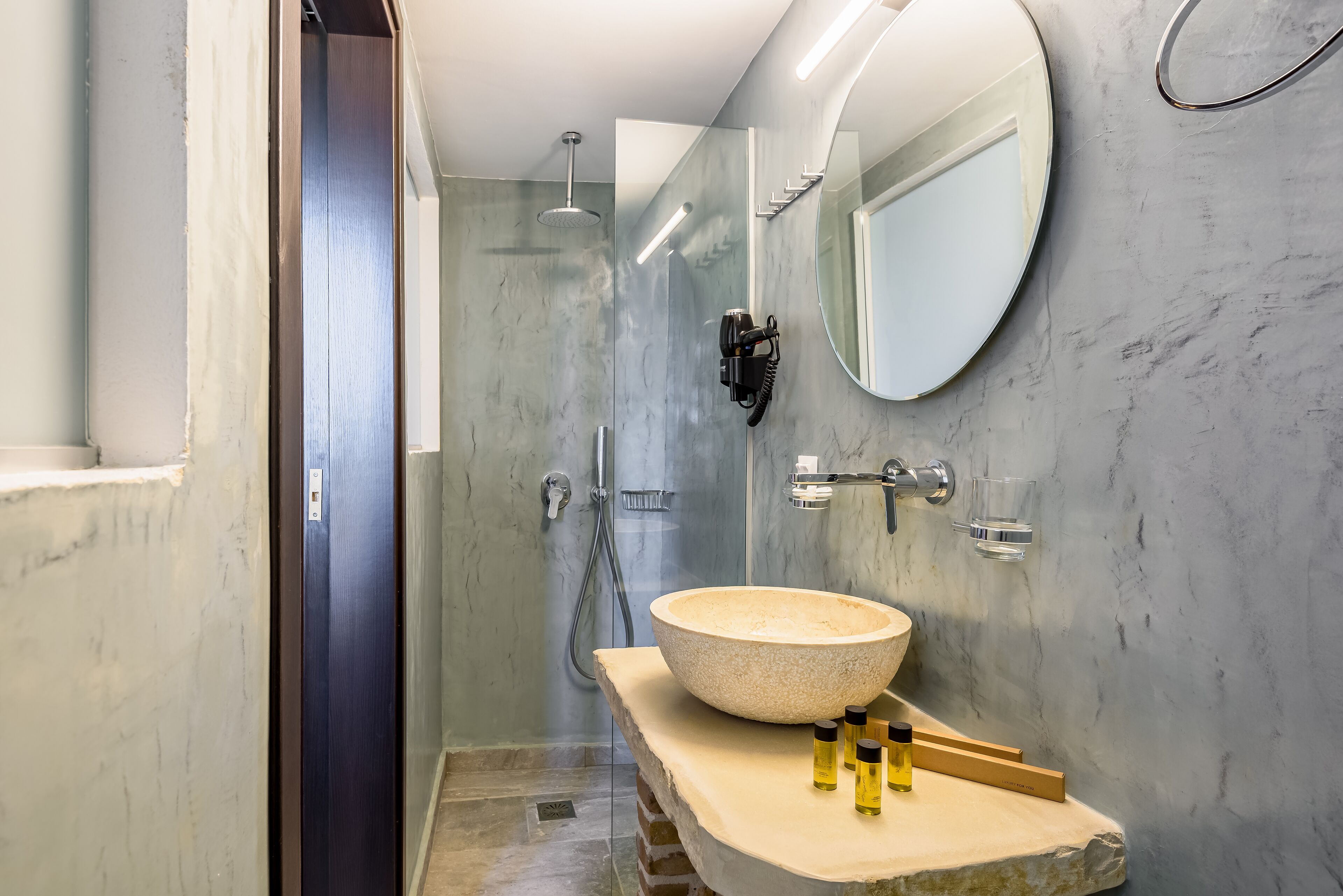 A modern bathroom with a large stone sink, a handheld showerhead, and a mirror.