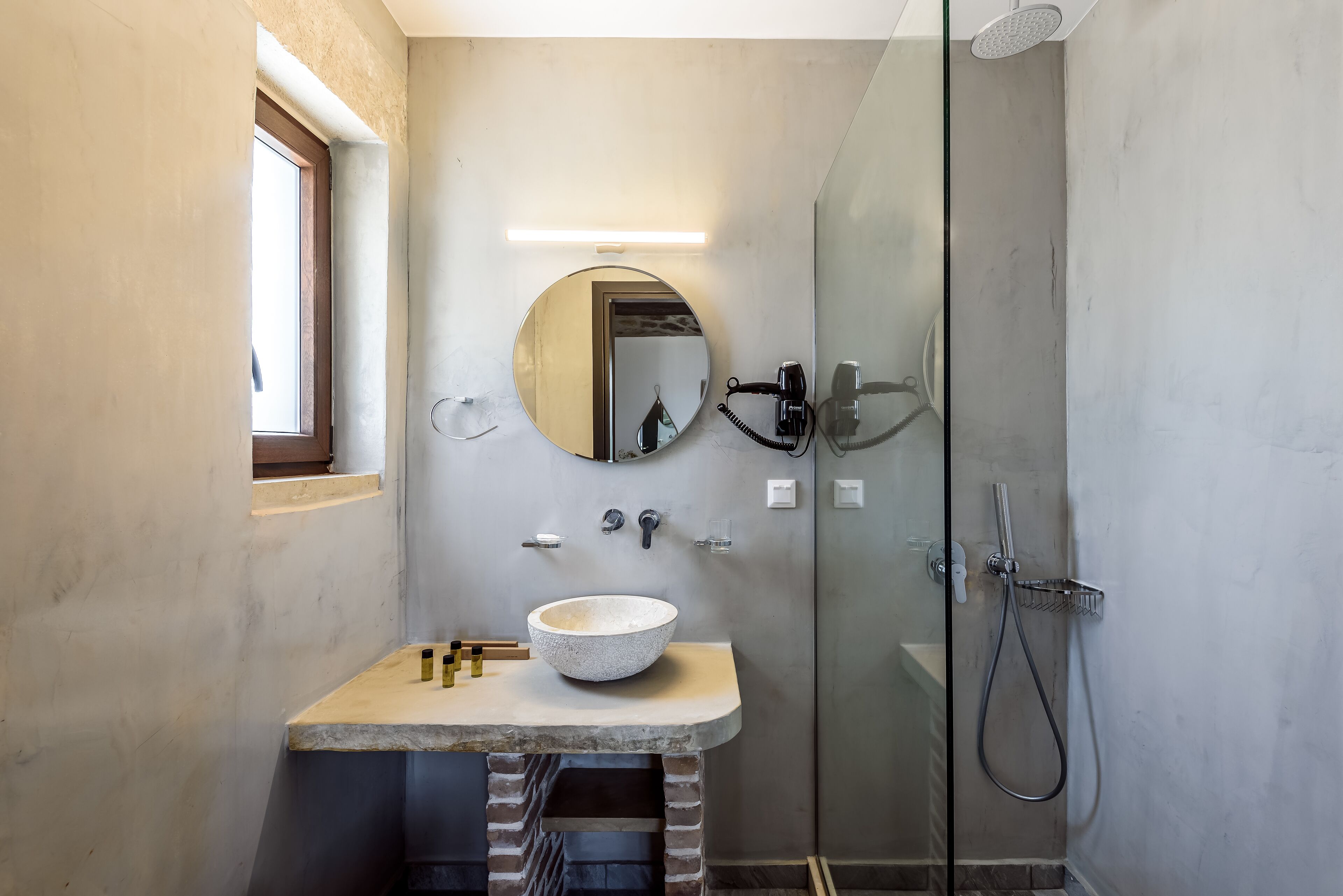 A modern bathroom with a stone sink, a round mirror, and a glass-enclosed shower.