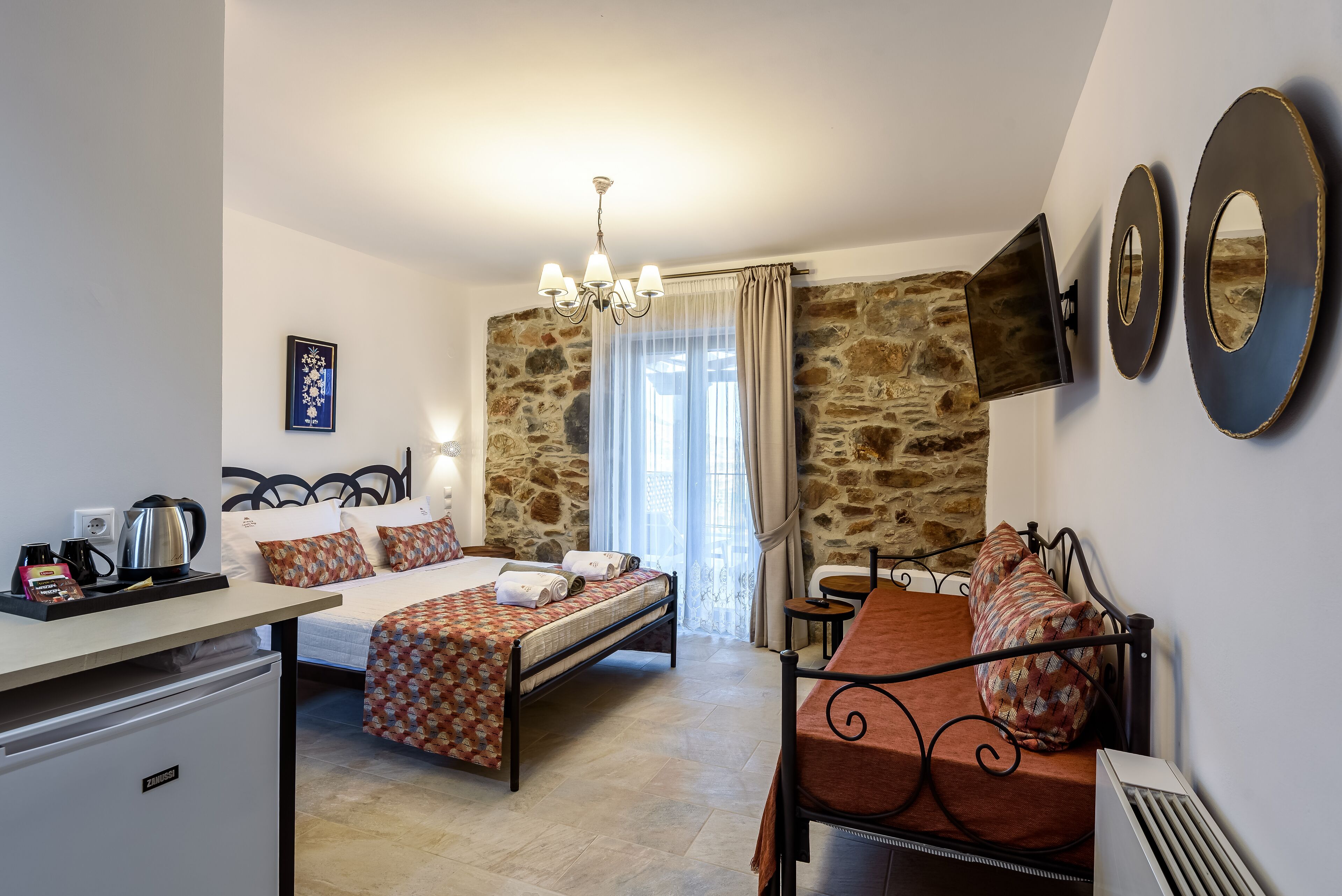 Une chambre d’hôtel avec deux lits, un coin cuisine, un mur en pierre et un téléviseur fixé au mur.