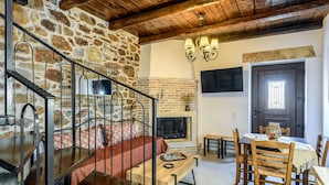 Una sala de estar acogedora con una pared de piedra, una chimenea, una mesa de comedor y una escalera con barandillas de metal.
