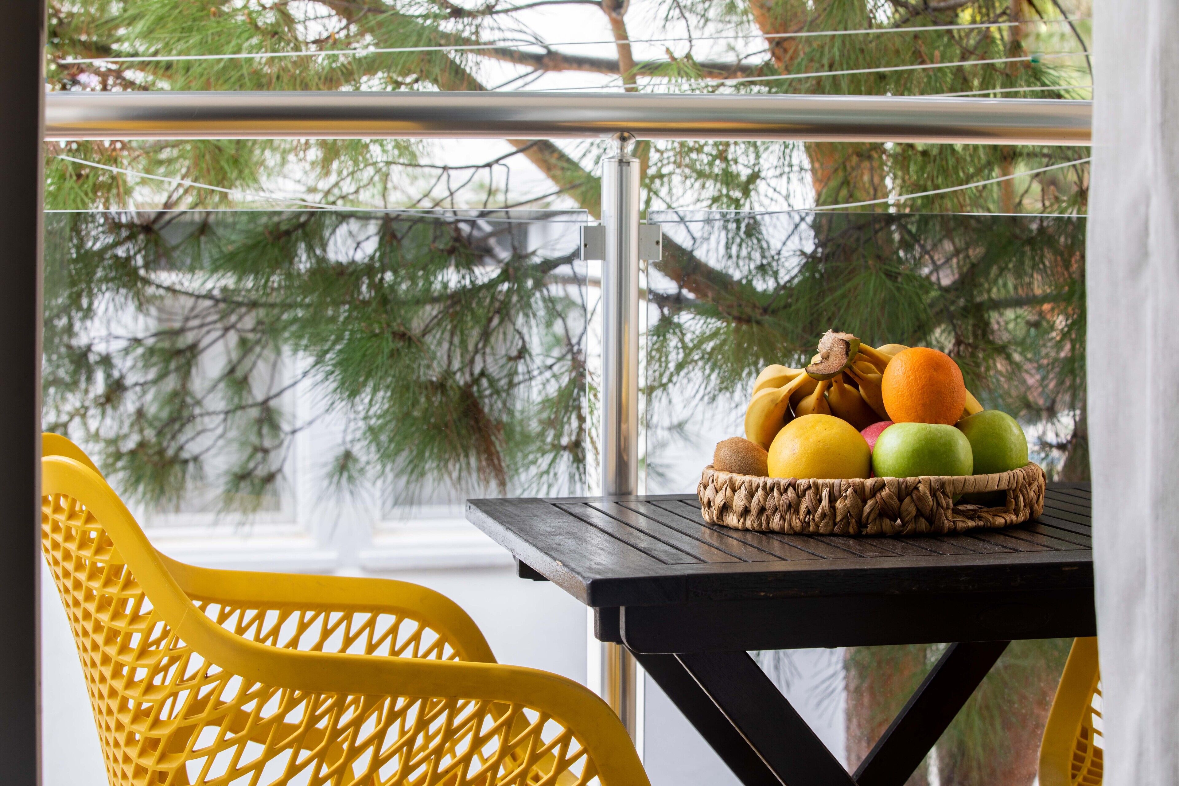 Una mesa con una cesta tejida llena de frutas y una silla amarilla.