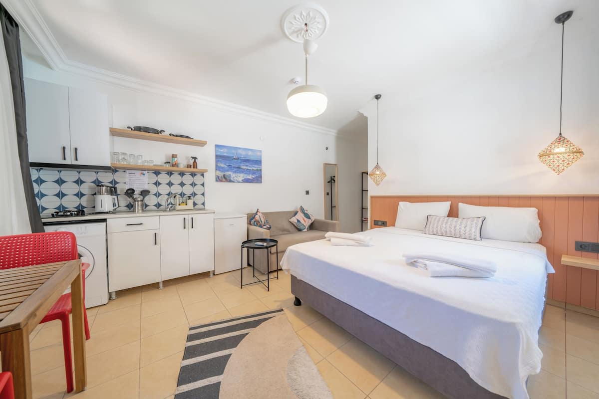 Een compacte hotelkamer met een bed, een klein keukentje, een zithoek en een badkamer.