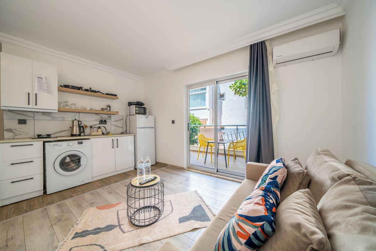 Een compacte keuken met een wasmachine, magnetron en een klein eethoekje met een tafel en stoelen.