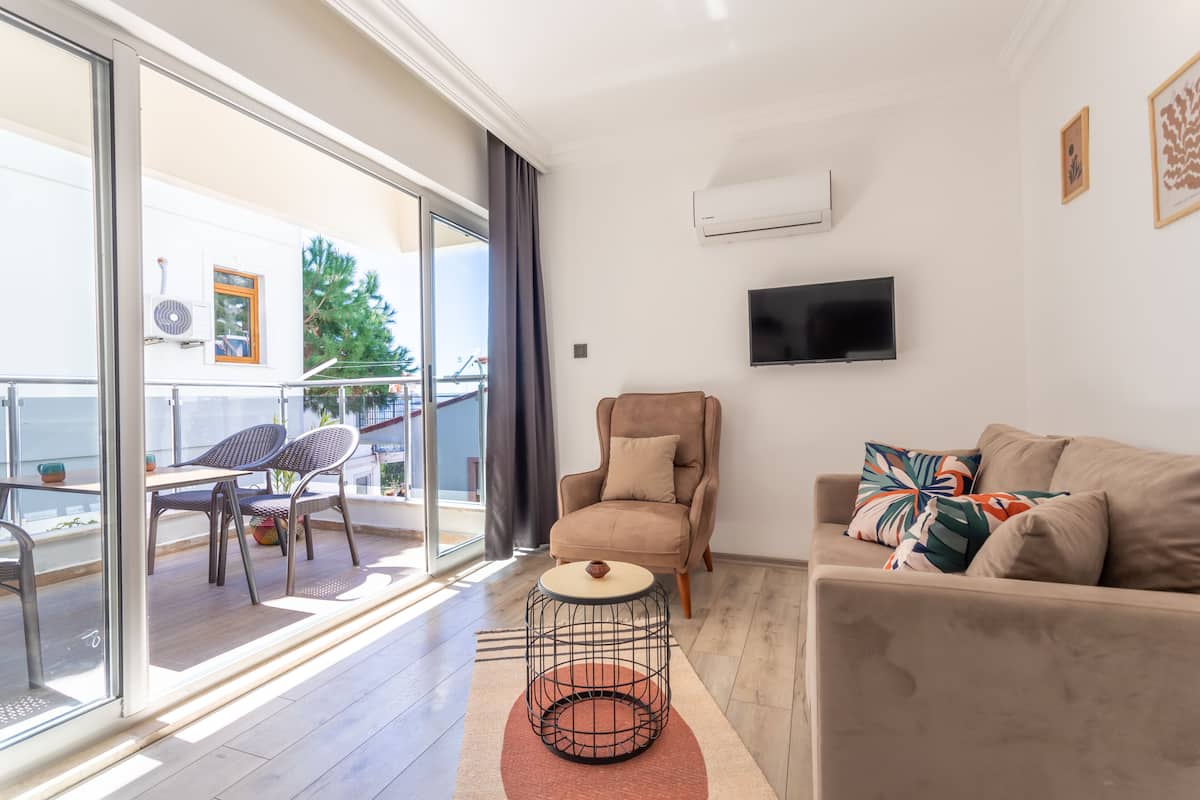Een moderne woonkamer met een bank, een stoel, een televisie en een balkon met stoelen en een tafel.