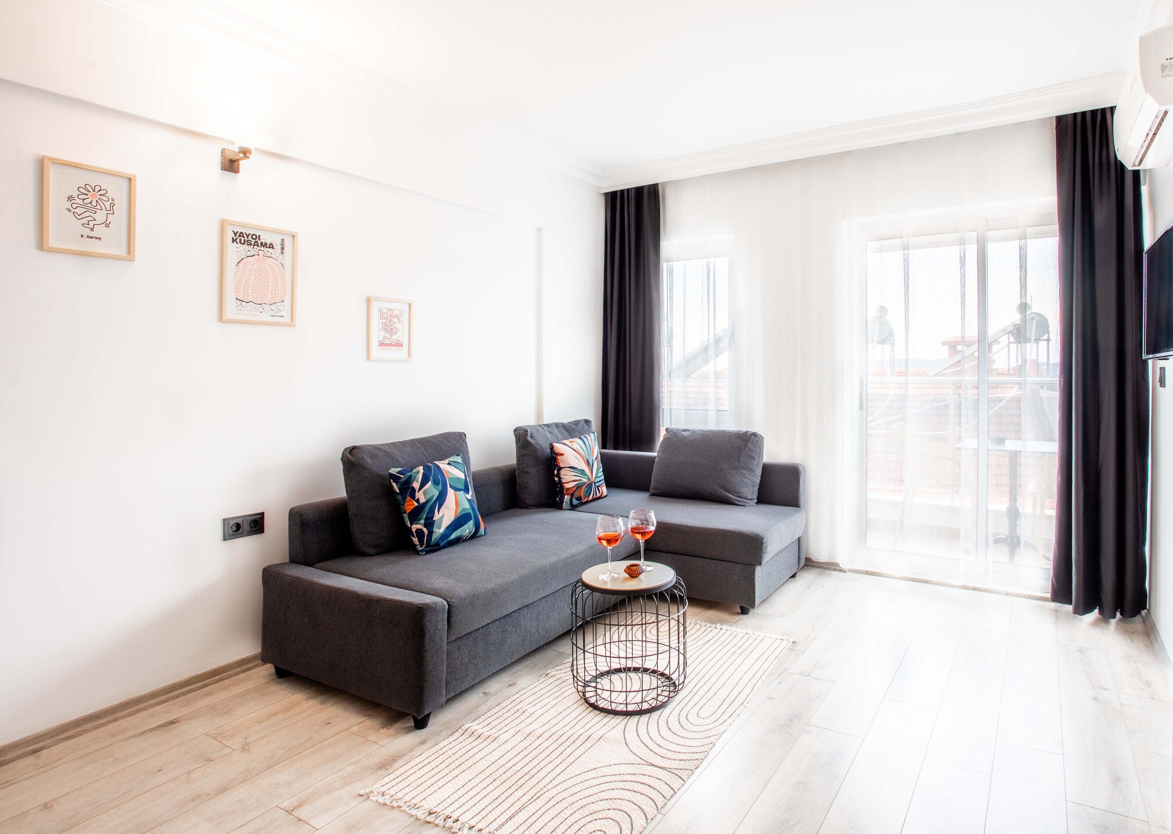 A modern living room with a grey sectional sofa, a round coffee table, and a large window with curtains.