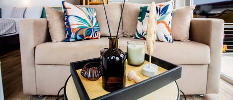 A modern living room with a beige sofa, colorful pillows, a tray with candles, and a bottle.