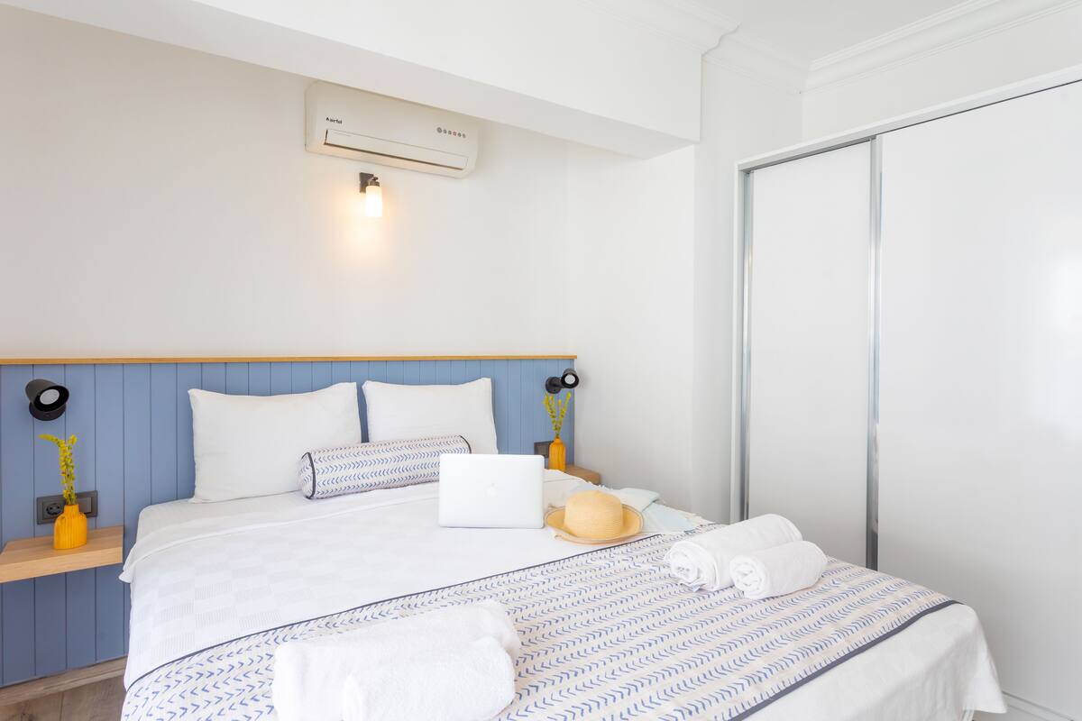 Een netjes ingerichte hotelkamer met een bed, nachtkastje met lamp en een wandairconditioner.