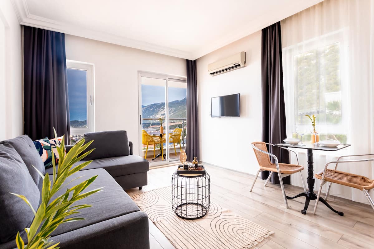 Een moderne woonkamer met een grijze bank, een ronde salontafel, en een eethoek met rieten stoelen en een kleine tafel.