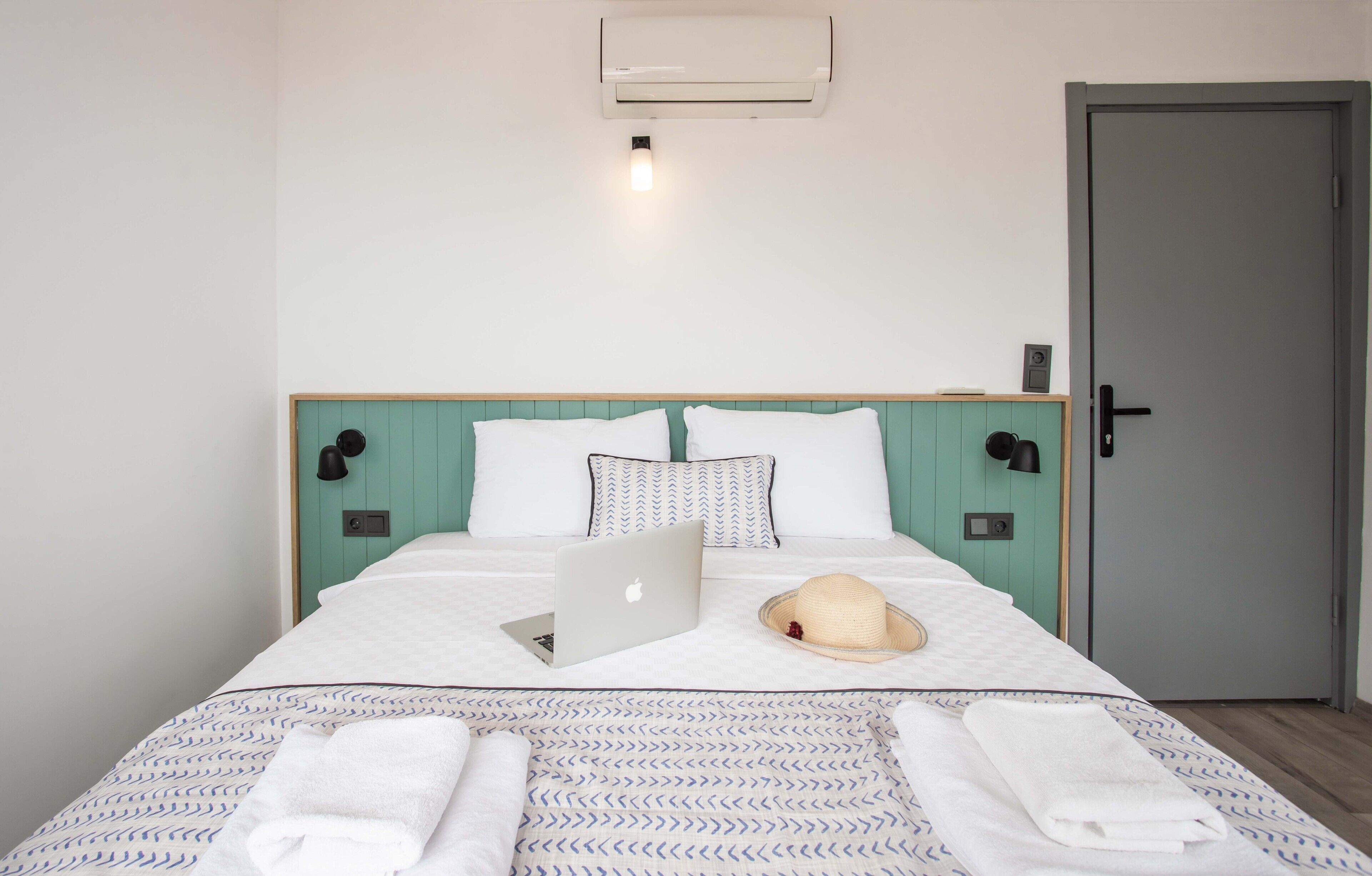 A neatly made bed with a laptop, a straw hat, and towels.