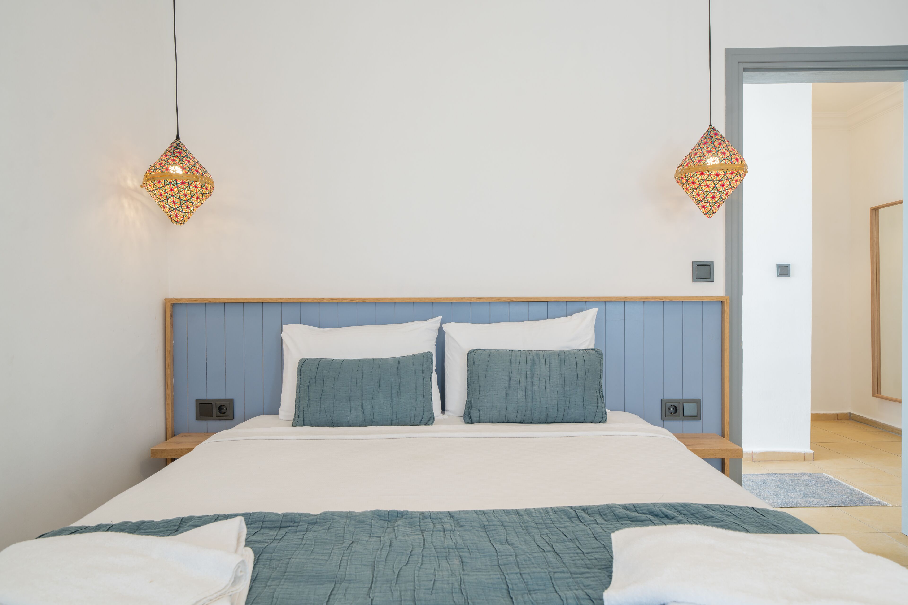 A bedroom with a bed, two bedside tables, a headboard, and two hanging lamps.