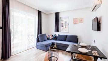 Un salon moderne avec un canapé d’angle, une table à manger et une grande fenêtre agrémentée de rideaux.