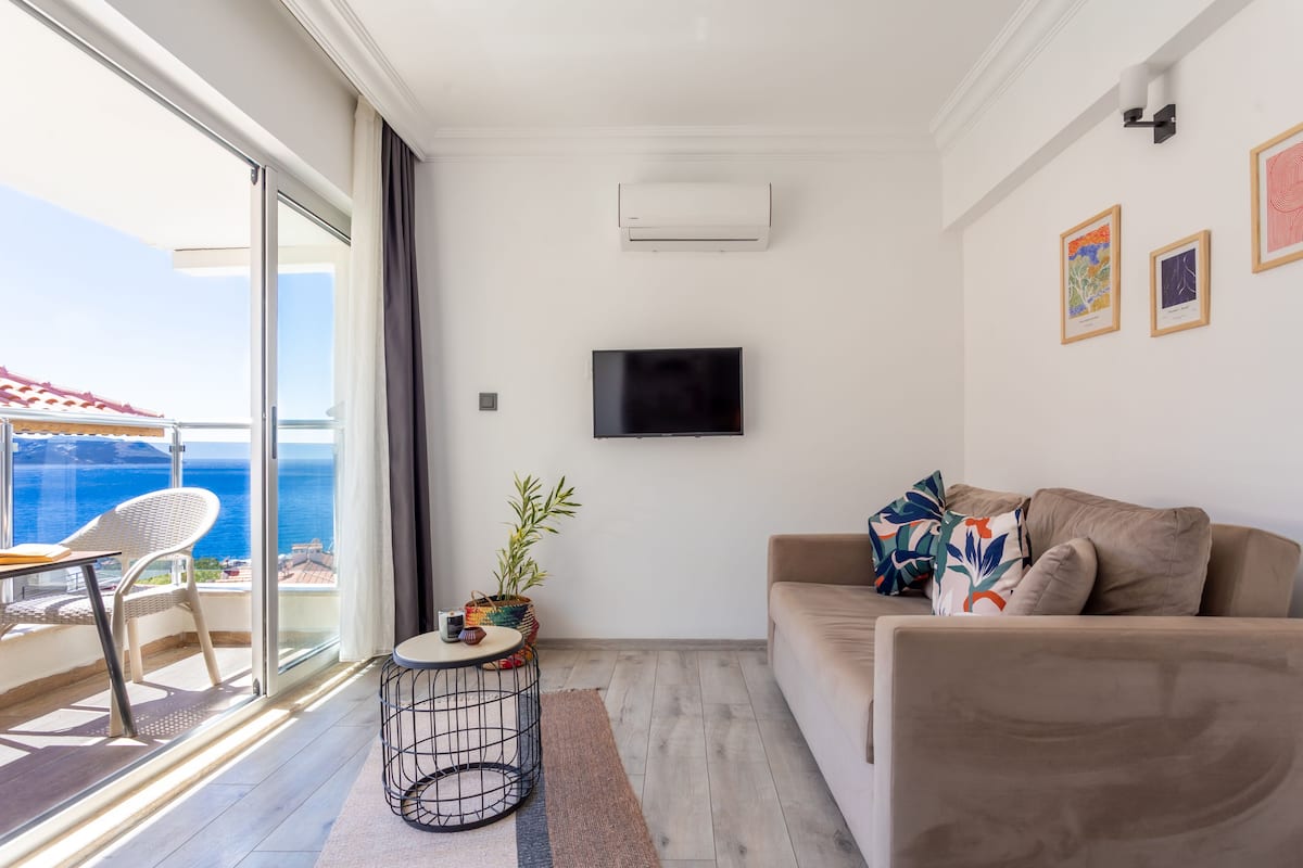 Een moderne woonkamer met een bank, een flatscreentelevisie en een klein tafeltje met een plant.