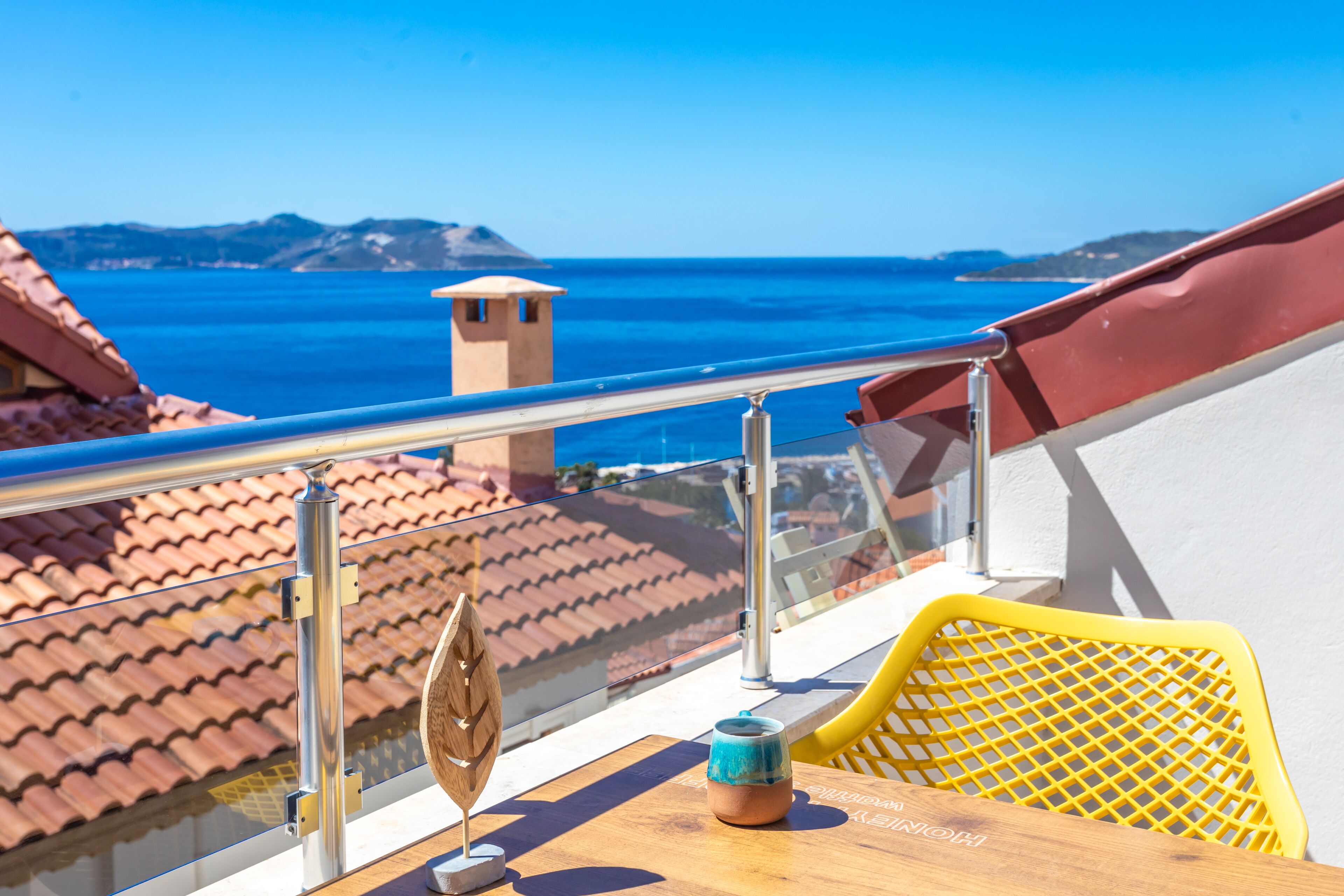 A balcony with a clear view of the sea, a wooden table, a yellow chair, and a small decorative item.
