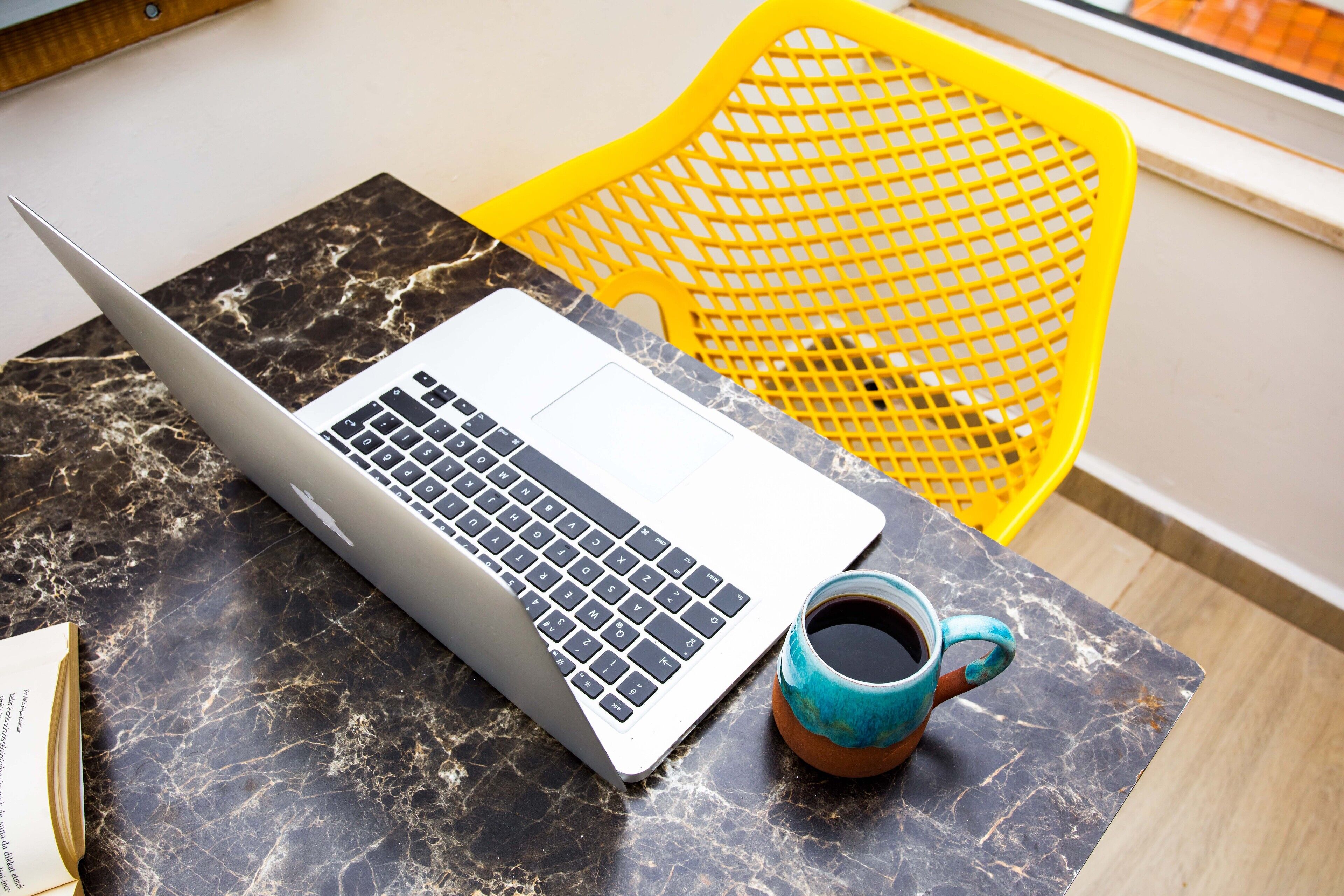 A laptop on a marble table, a coffee cup, and a yellow chair.