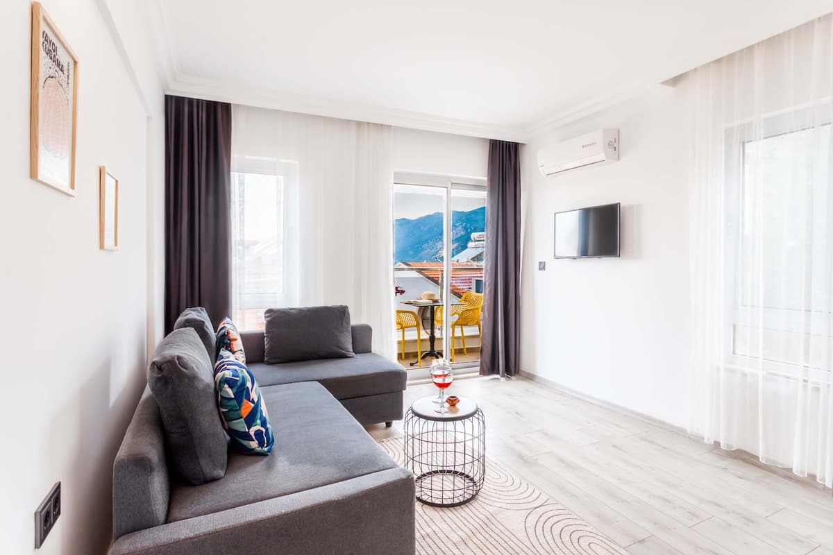 Een moderne woonkamer met een grijze bank, een klein rond salontafeltje en een aan de muur bevestigde televisie.