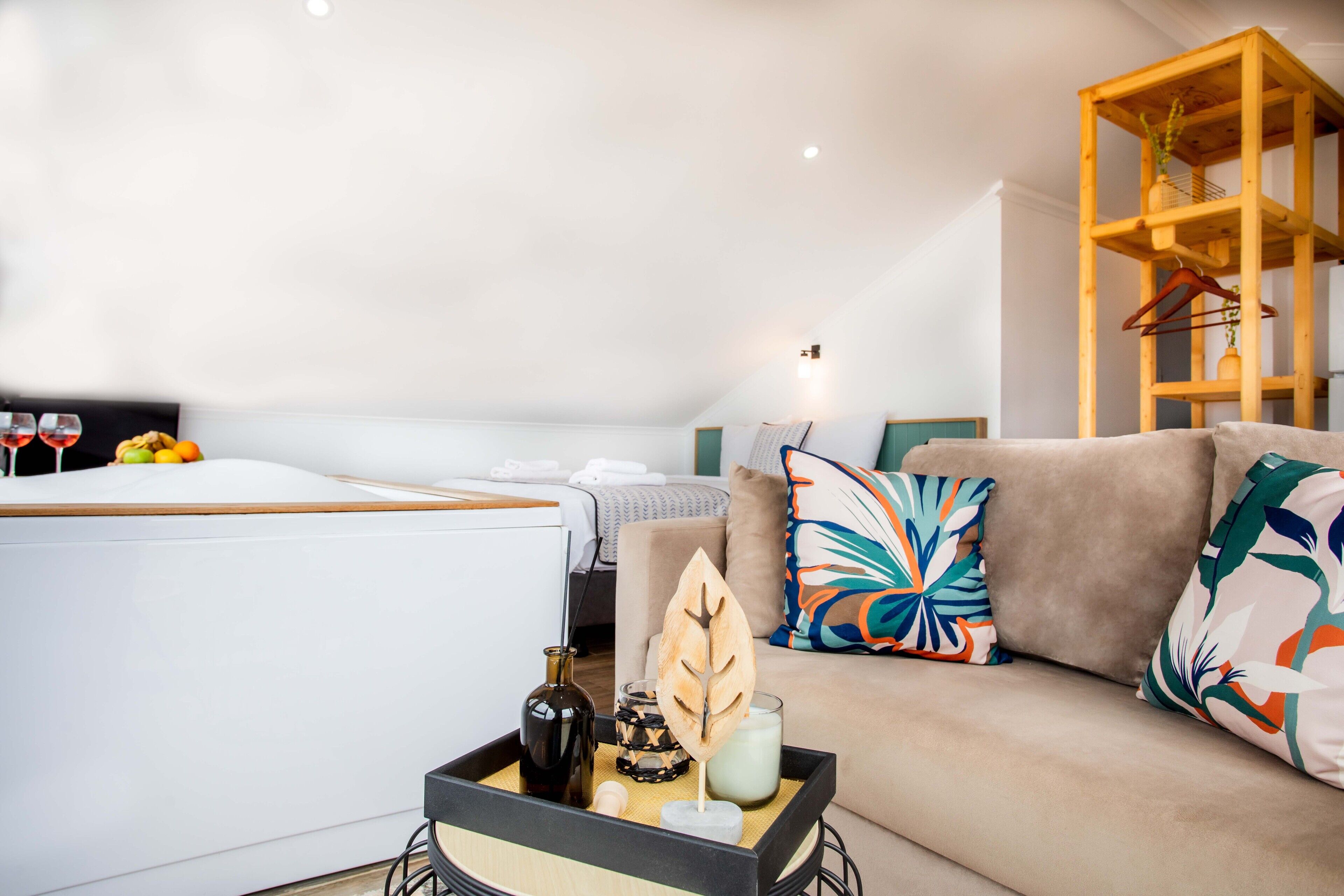 A modern living room with a sofa, a coffee table with decorative items, a wooden shelf, and a bed in the background.