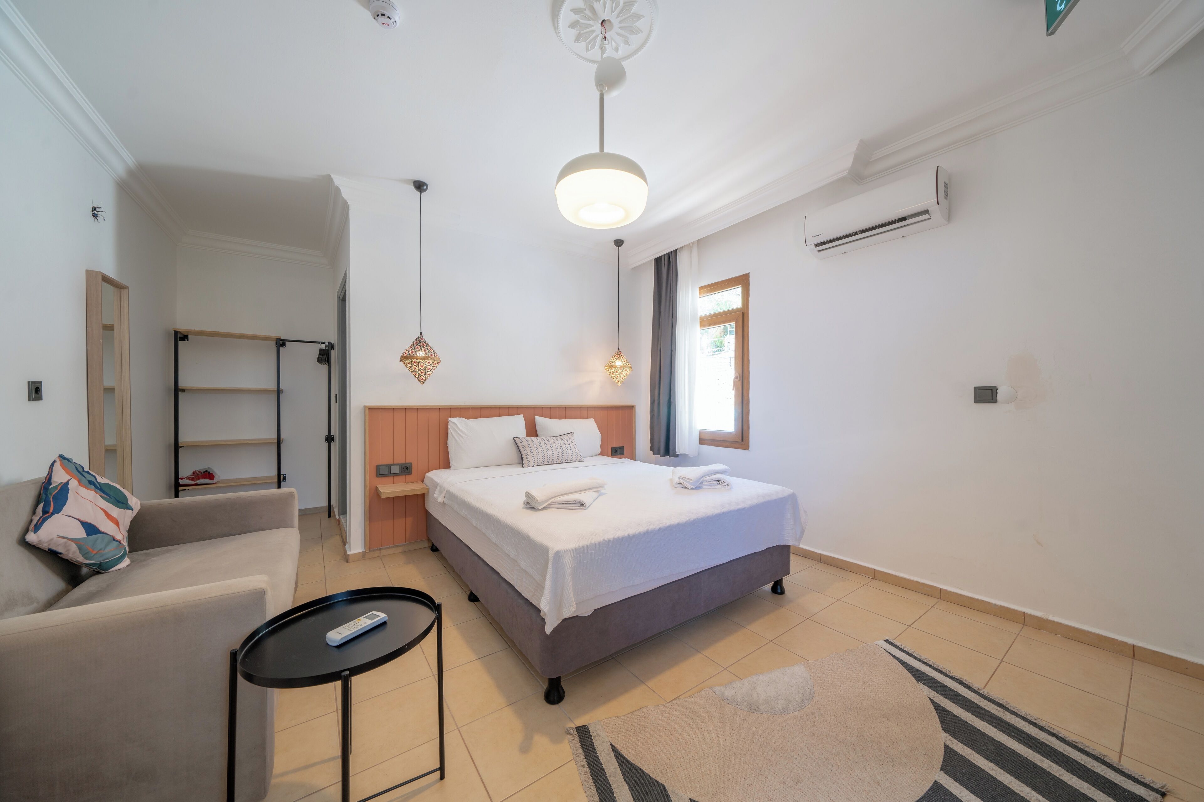 A modern hotel room with a bed, a sofa, a small table, and a hanging light fixture.