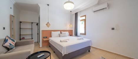 A modern hotel room with a bed, a sofa, a small table, and a hanging light fixture.