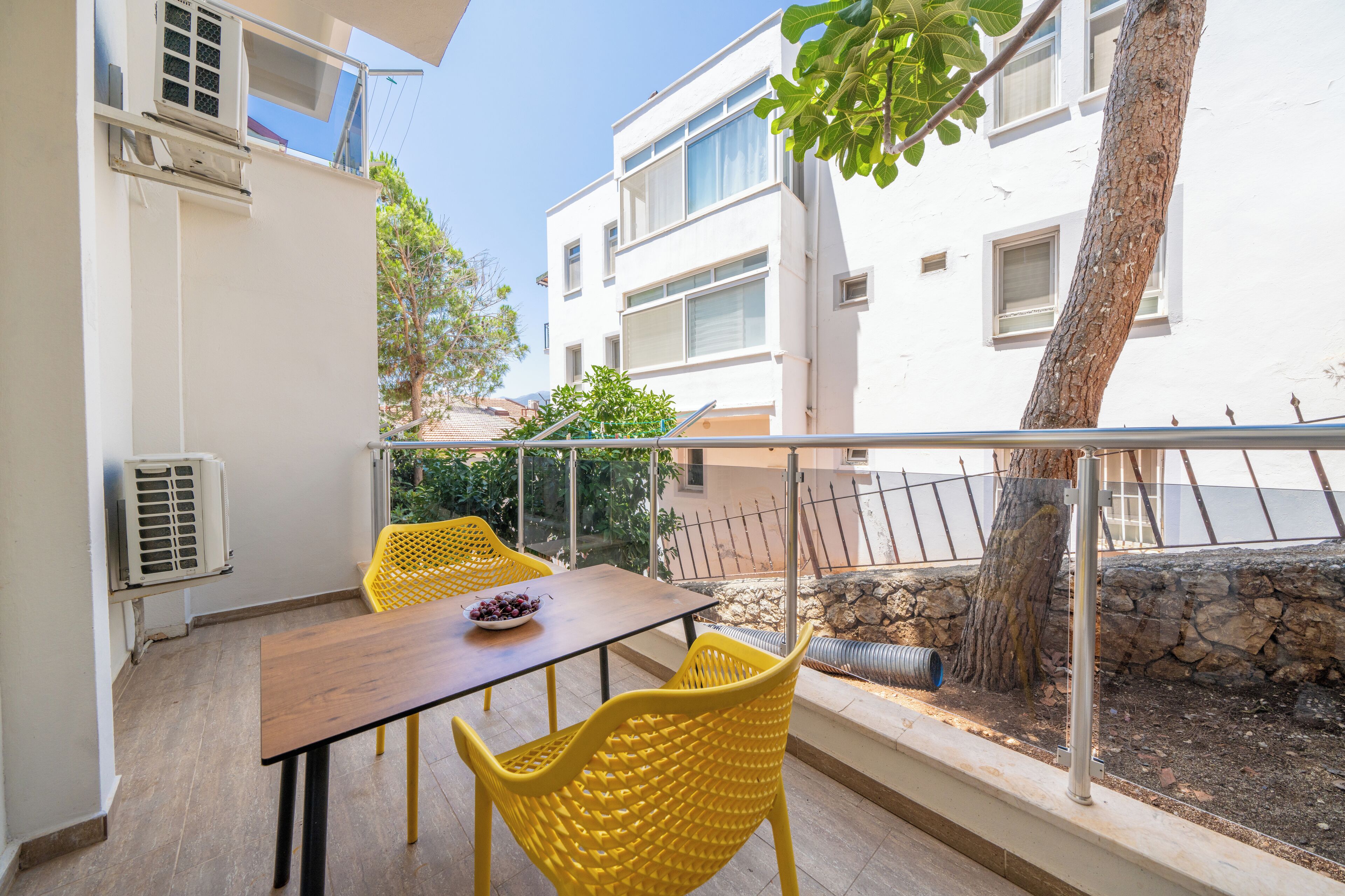 A balcony with a table and chairs, a view of a tree, and a building in the background.