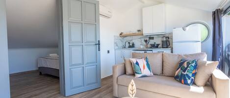 Una sala de estar moderna con un sofá, una mesita redonda y una zona de cocina con armarios y una ventana.