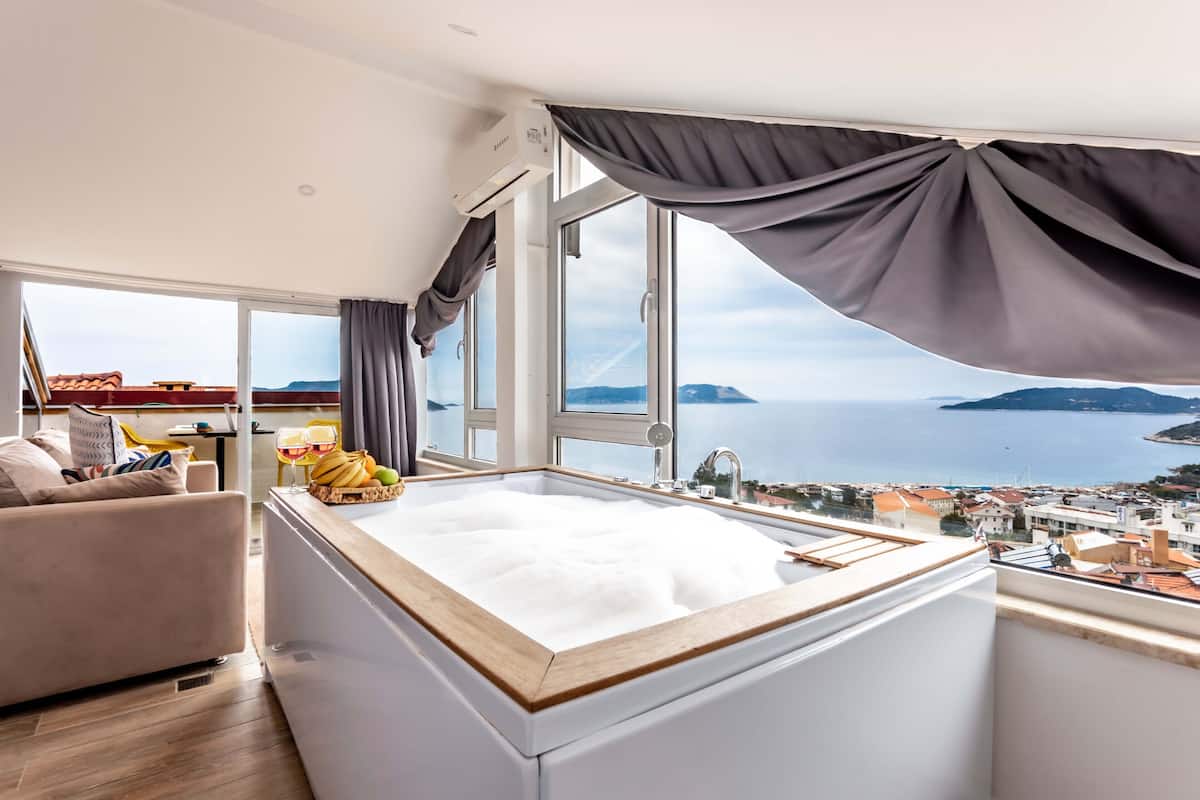 Een moderne kamer met een groot raam, een witte badkuip en uitzicht op zee en stad.