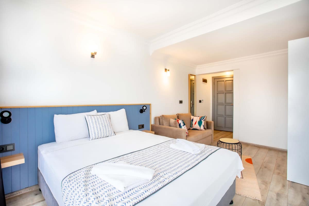 Een hotelkamer met een groot bed, een bank, een klein rond tafeltje en een deur die naar een andere kamer leidt.