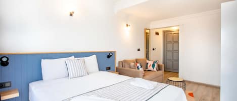 A hotel room with a large bed, a sofa, a small round table, and a door leading to another room.