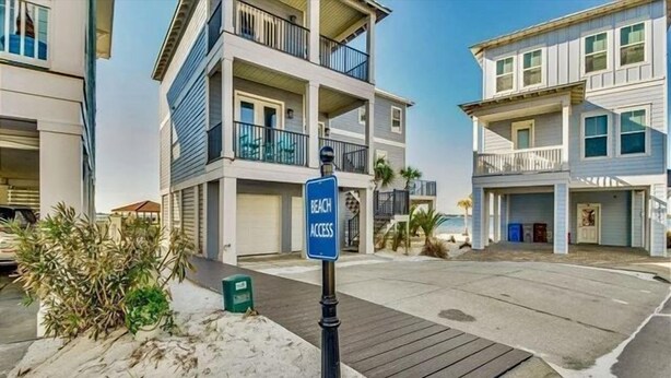 Um edifício residencial à beira-mar com um letreiro indicando 'Beach Access', uma área de estacionamento coberta e um calçadão de areia que leva à praia.
