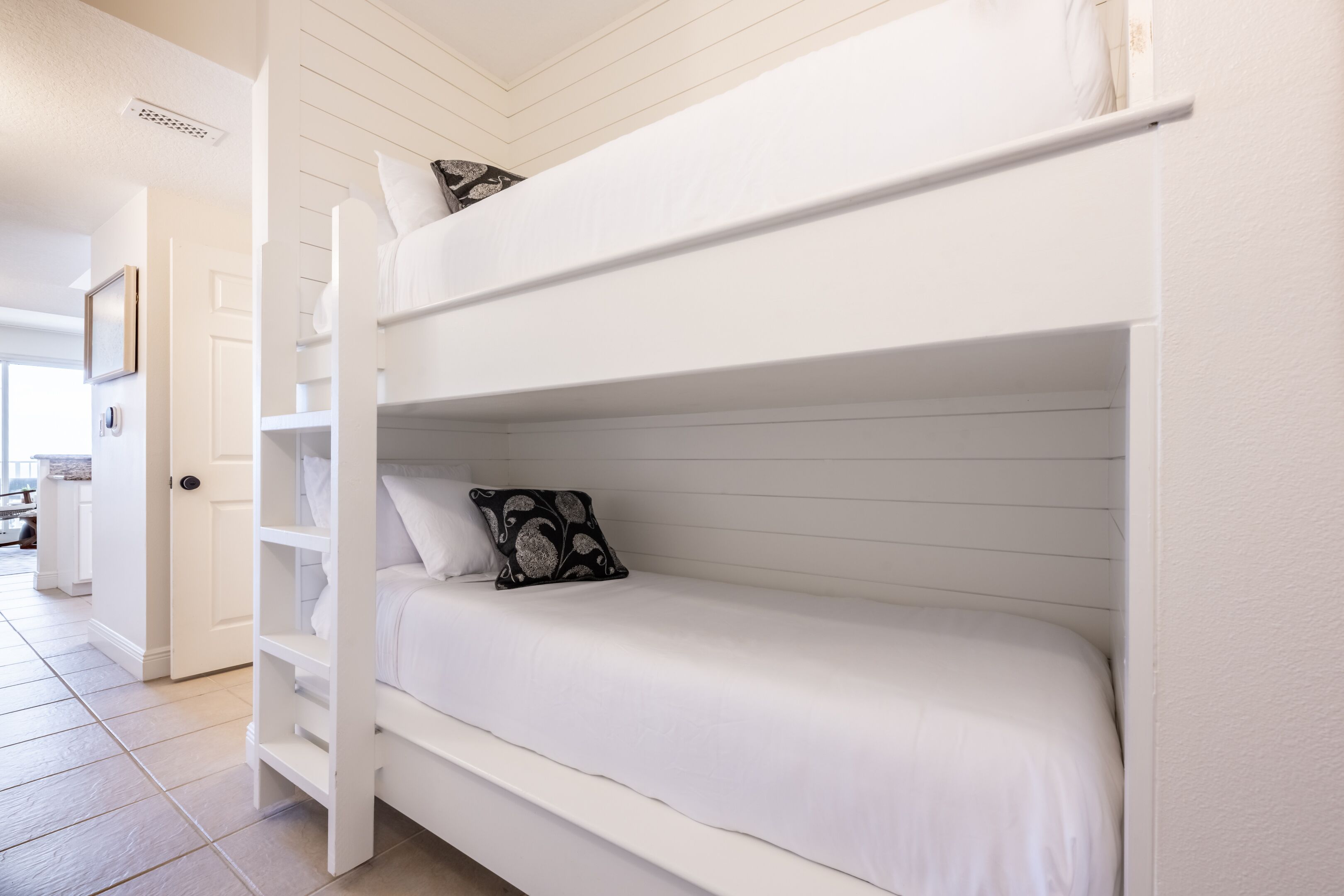 A bunk bed with white bedding and a black patterned pillow.