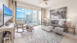 A spacious living room with a large TV, comfortable seating, a ceiling fan, and a balcony with a view of the ocean. - Seascape ~ Gulf View ~ Bunk Area (Miramar Beach)