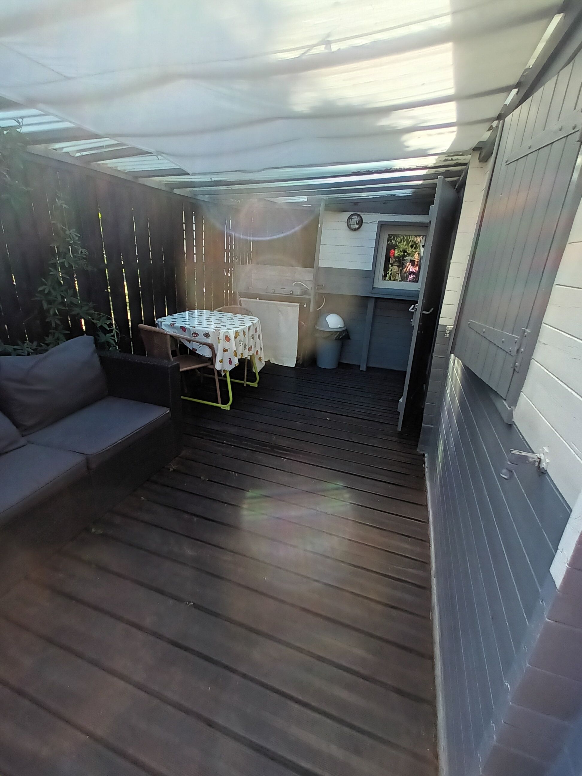 A covered patio with a table and chairs, a small kitchen area, and a wooden deck.
