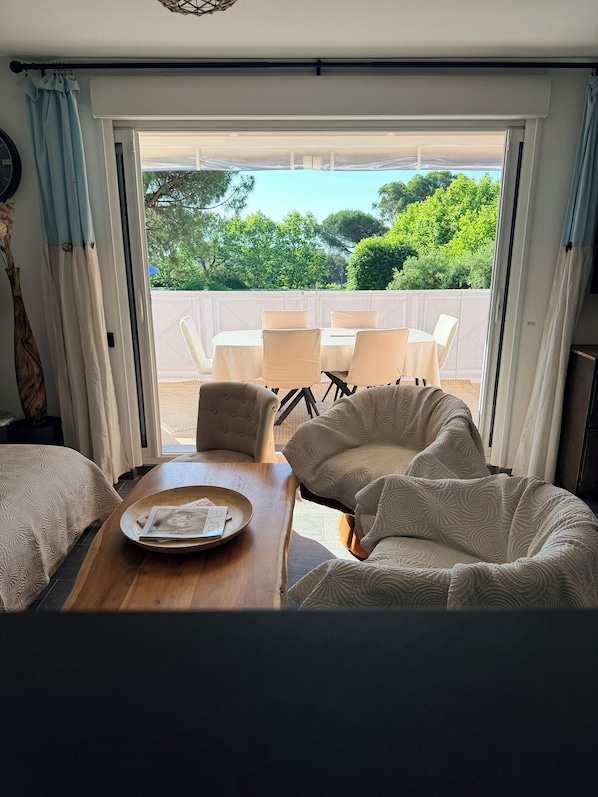 A room with a bed, a table with a tray, two chairs, and a view of a balcony with a table and chairs.
