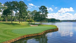 A golf course with a water body, trees, and a clear sky.