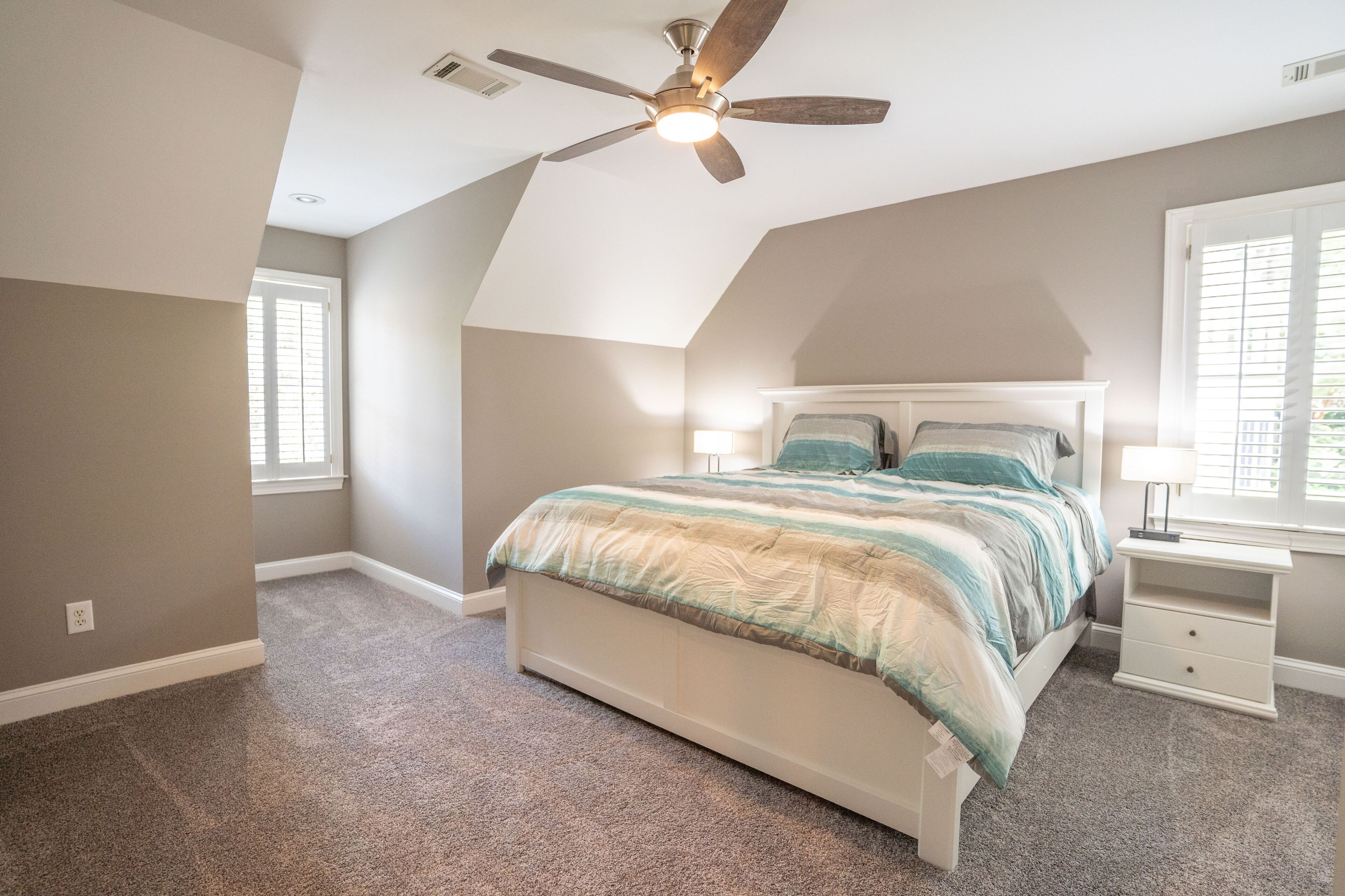 A bedroom with a bed, a nightstand, a ceiling fan, and a window.