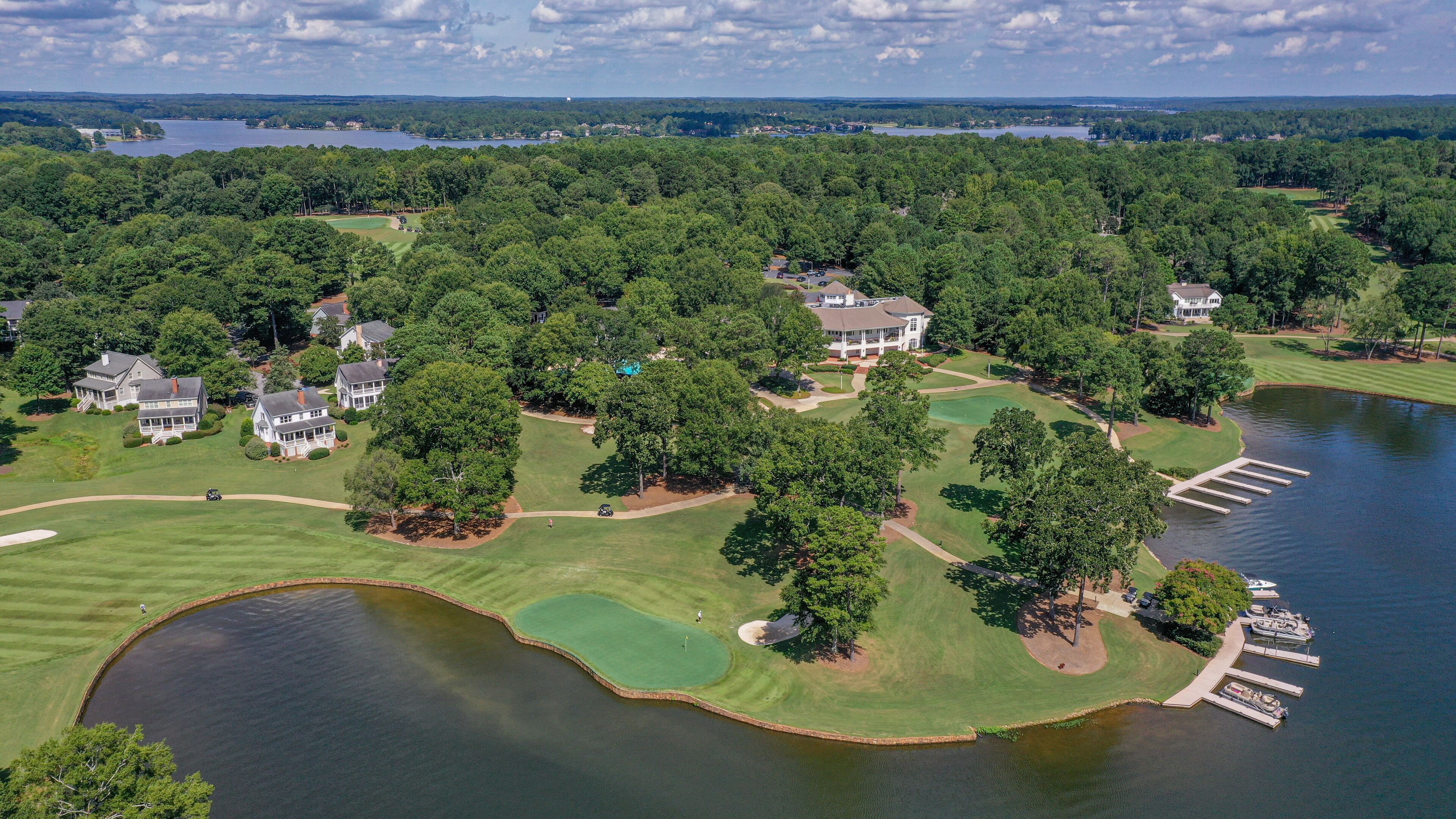 An aerial view of a golf course with multiple houses, a lake, and a dock.