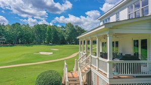 A golf course with a clubhouse featuring a covered porch and a staircase leading to the entrance.