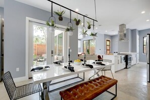 A modern kitchen with a central island, pendant lights, and hanging plants. - Premium East Austin Home | Hot Tub (Austin)