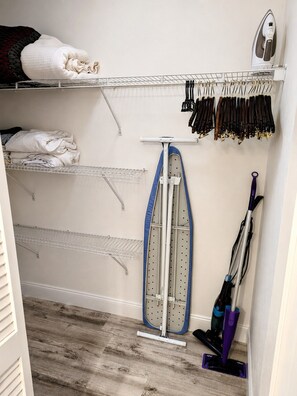 A laundry area with shelves for hanging clothes, a drying rack, an ironing board, and a vacuum cleaner. - Park Shore Resort-Top Floor BLDGJ #457 Water Views (Park Shore Resort)