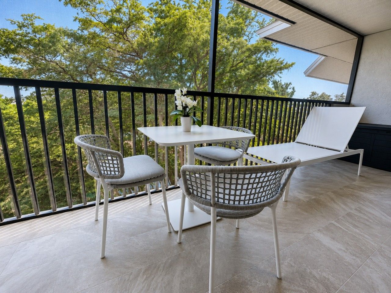 A balcony with a table and chairs, a potted plant, and a view of trees.