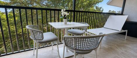 A balcony with a table and chairs, a potted plant, and a view of trees.