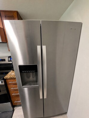 Un réfrigérateur Whirlpool en acier inoxydable, doté d’un distributeur d’eau, situé dans une cuisine avec des armoires en bois et un comptoir en granit.