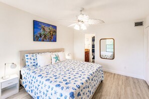 Une chambre à coucher avec un lit, un ventilateur de plafond, un tableau et un miroir.