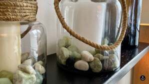 Dos frascos de vidrio con asas de cuerda, llenos de piedras y una vela, sobre una estantería.