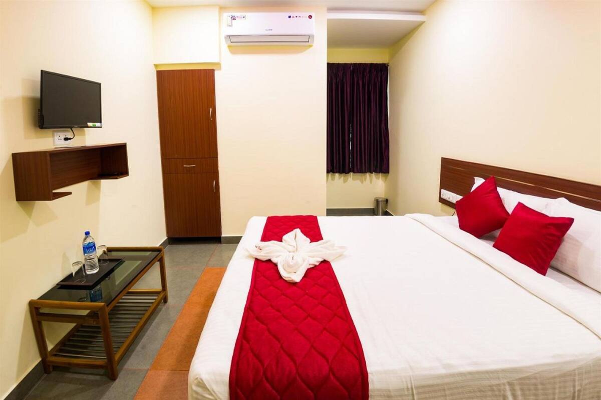 A hotel room with a bed, a TV, a wardrobe, and an air conditioning unit.
