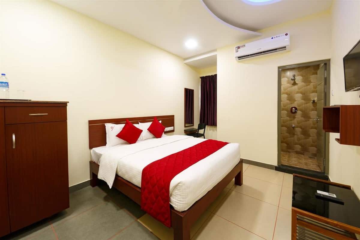 A hotel room with a bed, a wardrobe, an air conditioning unit, and a shower area.