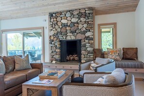 A cozy living room with a stone fireplace, leather sofas, and a coffee table with books.
