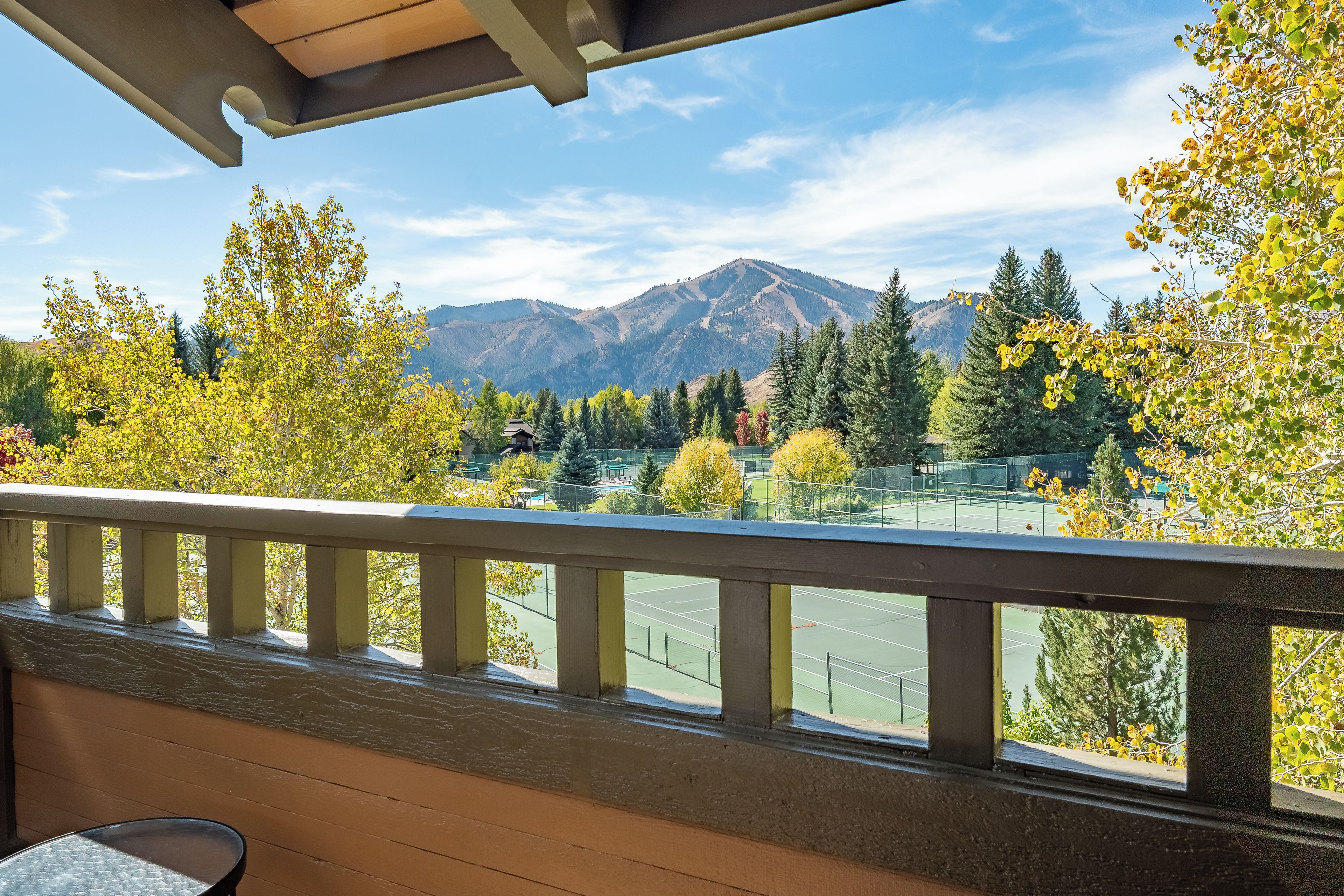A tennis court with a mountain view, a wooden deck, and a clear sky.