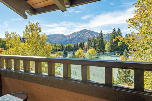 A tennis court with a mountain view, a wooden deck, and a clear sky.