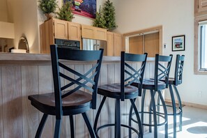 A kitchen with wooden cabinets, a stainless steel refrigerator, and a bar area with four black chairs.